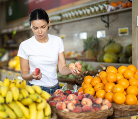 Focused positive woman shopping in organic food store, choosing flat peaches