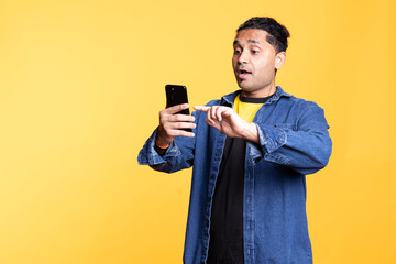 Relaxed Indian man with man bun uses smartphone browsing online apps, smiling calmly and standing...