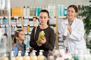 Mom and daughter standing in pharmacy and choosing medicated shampoo for hair treatment against the background of 