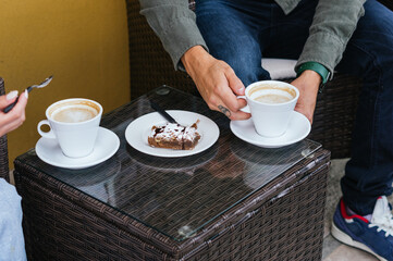 A person is sitting at a table with a plate of dessert and two cups of coffee