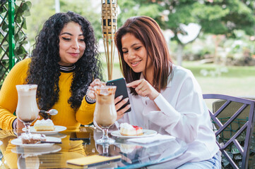 Young Hispanic women enjoying coffee and desserts while looking at a phone