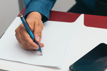 A person is writing on a piece of paper with a blue pen