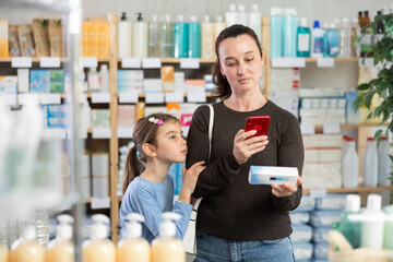Adult woman with daughter buyers scanning qr code for box of ointment in pharmacy