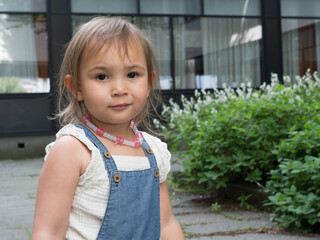 Portrait of young girl wearing denim dress and necklace outdoors in natural light