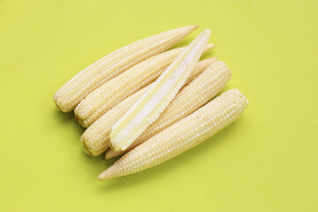 Fresh baby corns arranged on a vibrant yellow background.