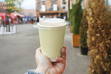 paper creamy color cup of drink in women's hand on evening street