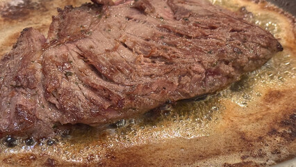 A beef steak searing in a hot pan with bubbling butter
