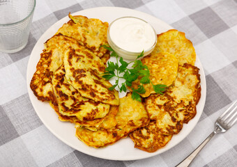 Delicious zucchini pancakes with bowl of sour cream served on plate