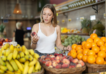 Young woman buyer choosing fresh flat peaches in vegetable shop