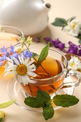 Aromatic herbal tea in glass cups, different flowers, mint and teapot on beige background, closeup