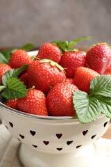 Fresh ripe strawberries and leaves in metal colander on table, closeup