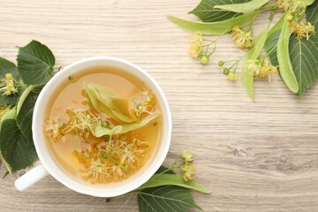 Fresh linden tea in cup and flowers on wooden table, flat lay. Space for text