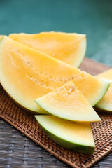 Pieces of ripe yellow watermelon on wicker table near swimming pool, closeup
