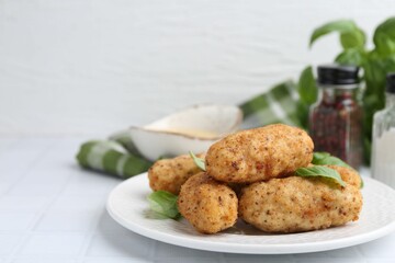Tasty fried croquettes and basil on white tiled table, closeup. Space for text