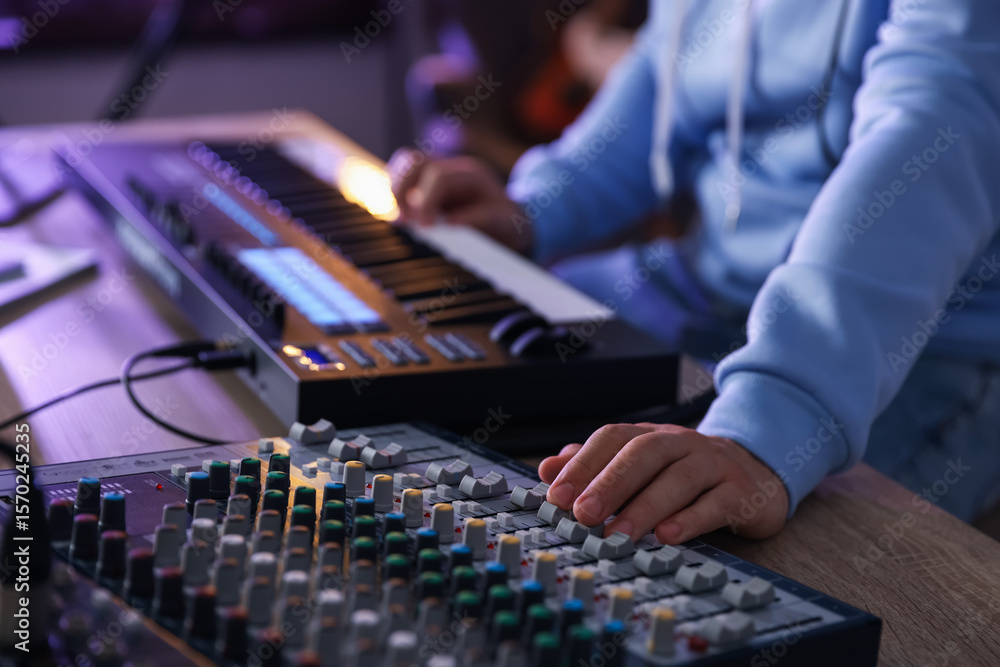 Poster man working with midi keyboard and dj mixer at wooden table in home studio, selective focus