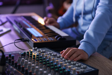 Man working with MIDI keyboard and dj mixer at wooden table in home studio, selective focus