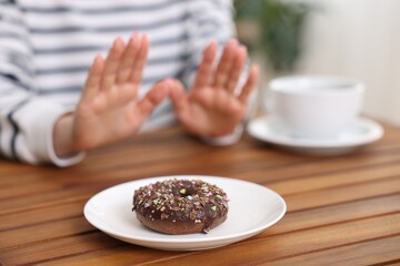 Gluten free diet. Woman refusing from donut at wooden table indoors, selective focus