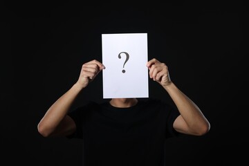 Man hiding behind paper sheet with question mark on dark background