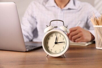 Deadline. Alarm clock and man working at wooden table, selective focus