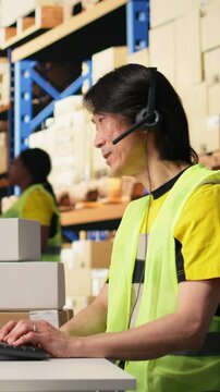 Vertical Video Call center male worker answer help line calls in a logistics warehouse, updating clients on orders and resolving cargo mix ups. Managing shipping software and airway bills. Camera A.