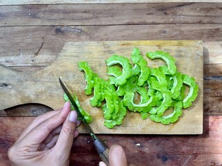 a woman's hand is slicing bitter melon vegetables on a wooden chopstick using a small knife, the...