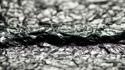 Closeup sequence of wrinkled reflective silver foil surface shifting and changing texture under - Powered by Adobe