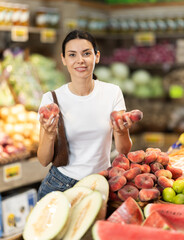 Woman stands in a supermarket near a bountiful fruit counter and chooses a flat peach. Customer prepares to weigh the fruit before buying