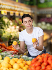Woman near vegetable stand in store choose peach. Client view ripeness of fruit, take out fruits...