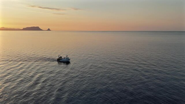 Peschereccio in navigazione nel golfo di sferracavallo accarezzato dal sole al tramonto durante una battuta di pesca estiva al gambero rosso di mazzara del vallo vista dall'alto con drone sky line