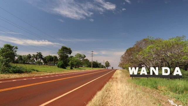 Panoramic shot from Route 12 in Wanda, Misiones. Features the pristine road, lush vegetation, and the corporeal sign welcoming visitors to the city.