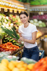 Woman in casual clothes chooses bunches of fresh green onions. Customer came to a vegetable shop for greens to cook breakfast