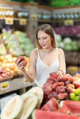 Woman near vegetable stand in store choose flat peach. Client view ripeness of fruit, take out...