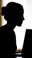 Silhouette of a woman seated at a laptop.