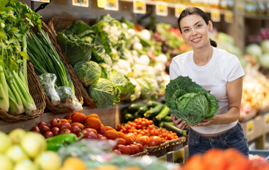 Woman near vegetable stand in store choose cabbage. Client view examine ripeness of fruit, take out...