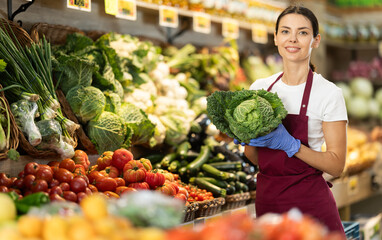Female grocery store worker offers ripe broccoli cabbage in grocery department of the supermarket