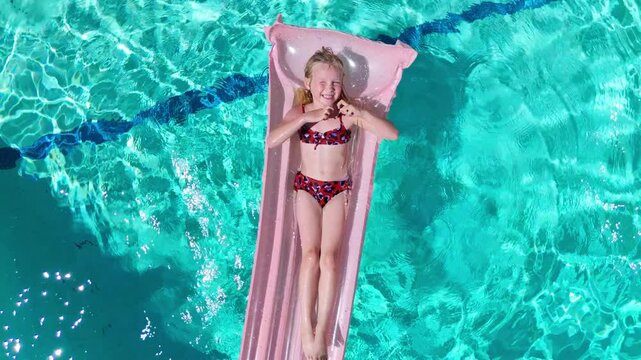 Slow motion top-down shot of smiling girl making heart shape on pink float in pool