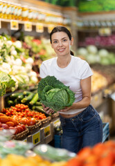 Woman near vegetable stand in store choose cabbage. Client view examine ripeness of fruit, take out...