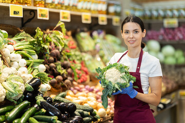 Female grocery store worker offers ripe broccoli cabbage in grocery department of the supermarket
