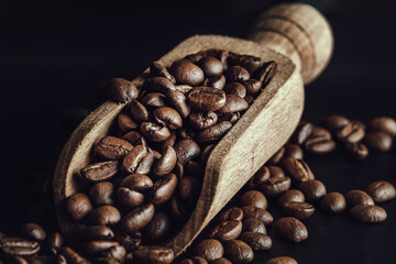 View of Roasted coffee beans on a rich textured surface in Wooden coffee scoop on black background....