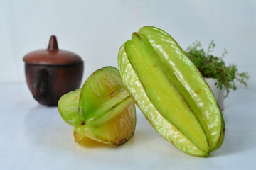 Fresh starfruit (carambola) slices with a whole fruit, styled in a clean setup with clay pot and...