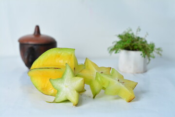 Fresh starfruit (carambola) slices with a whole fruit, styled in a clean setup with clay pot and...