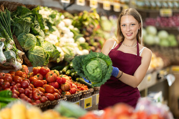 Female grocery store worker offers ripe broccoli cabbage in grocery department of the supermarket