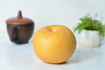Close-up of a fresh Asian pear on white background with traditional clay pot and potted herb....