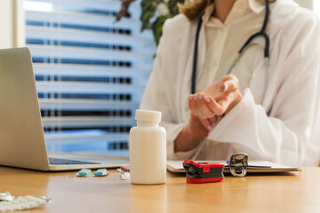 A doctor demonstrates to a patient in an online meeting how to measure a pulse. Mock-up of a pill 