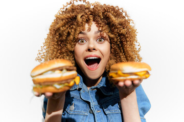 Happy young woman with curly hair showcasing two delicious burgers, expressing joy and excitement...