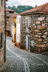 Picturesque cobblestone street winds through the historic town of Tarouca. Portugal. Showcasing traditional stone houses with tiled roofs and a glimpse of the lush green landscape in the background