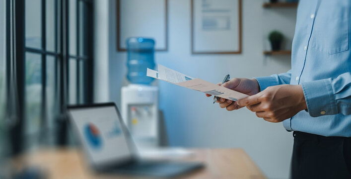 Person holds documents near laptop and water cooler in an office setting.