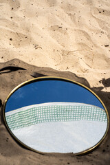 Round mirror on sandy surface reflecting towel and sky