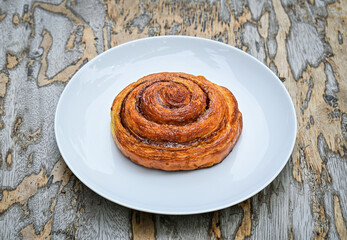 close up view of one sweet Cinnamon roll dessert on white plate. Isolated on wooden table background. 