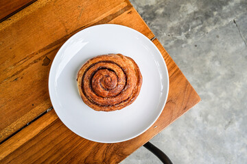 Top view of one sweet Cinnamon roll dessert on white plate with fork and knife. wooden table background. high angle, above, close up. corner.